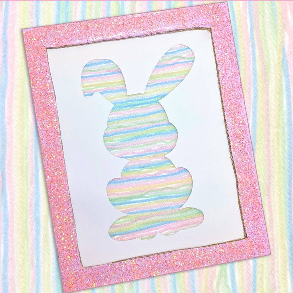 A bunny silhouette on a piece of cardboard made with rainbow pastel yarn.