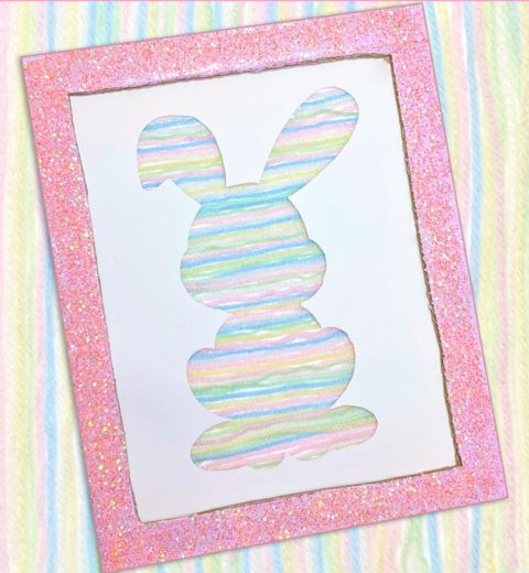 A bunny silhouette on a piece of cardboard made with rainbow pastel yarn.